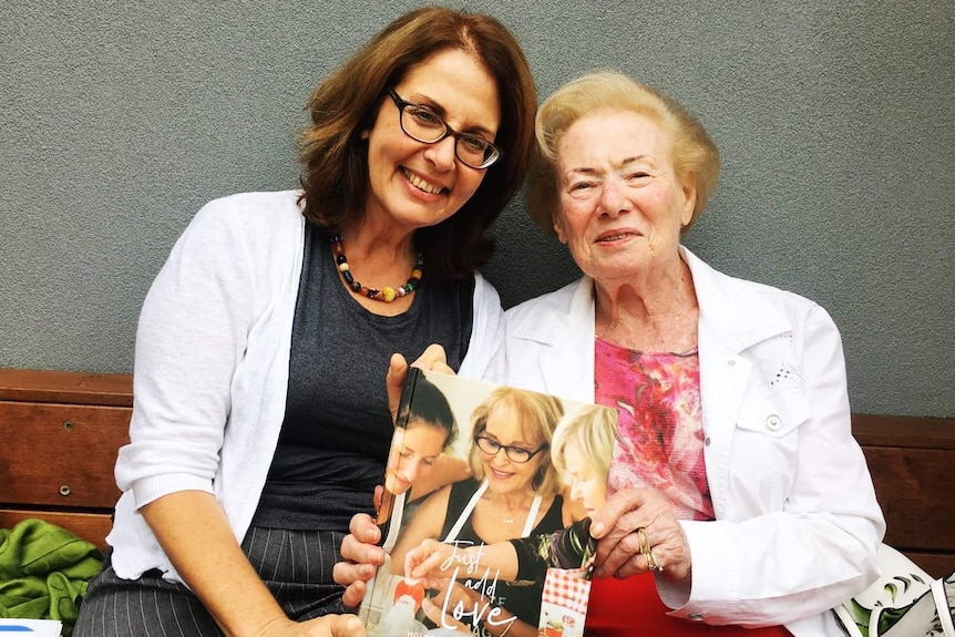 A younger woman in glasses and an older woman embrace and hold a book