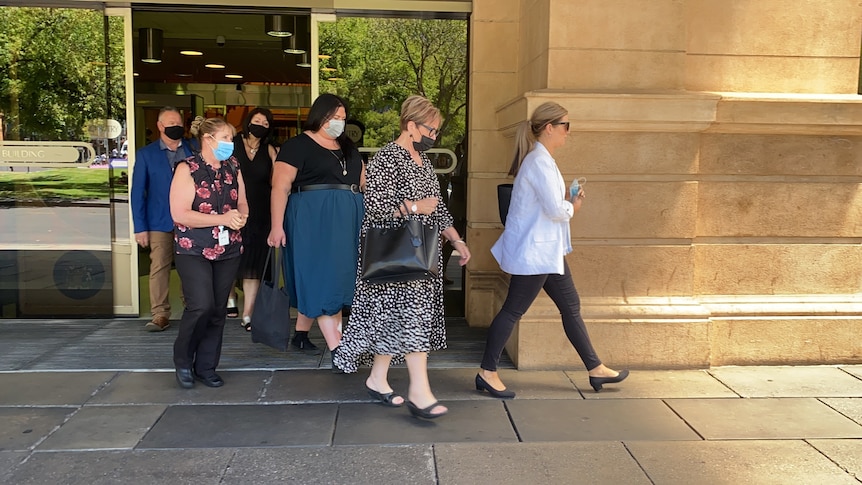 A group of people are walking out of glass sliding doors exiting a court building