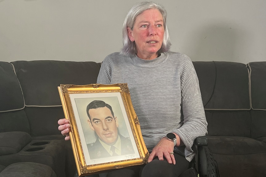 Andrea Brown sits on a couch as she speaks to a reporter and holds up a portrait of her father