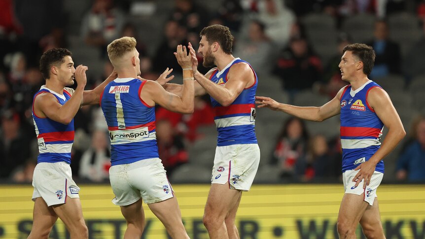 Four AFL players wearing red, white and blue, come together to celebrate a goal