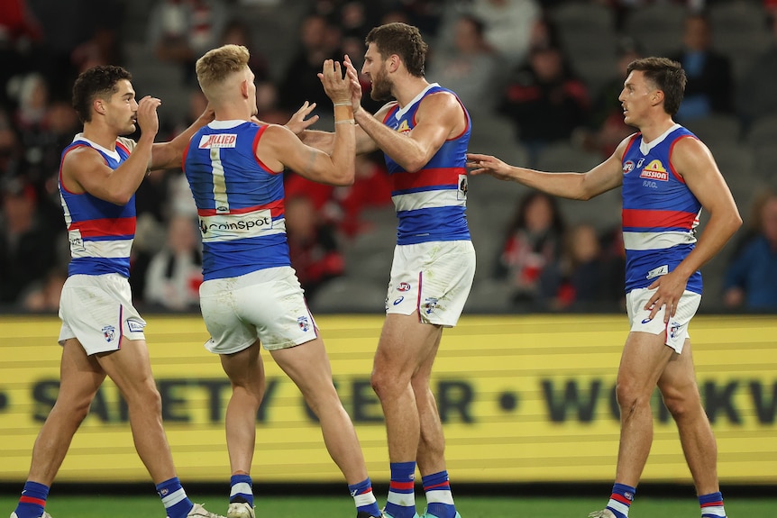Four AFL players wearing red, white and blue, come together to celebrate a goal