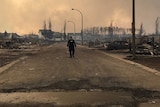 Man stands alone in street, surrounded by burned homes and cars