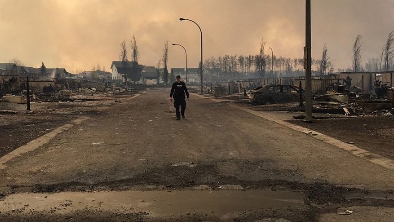 Man stands alone in street, surrounded by burned homes and cars