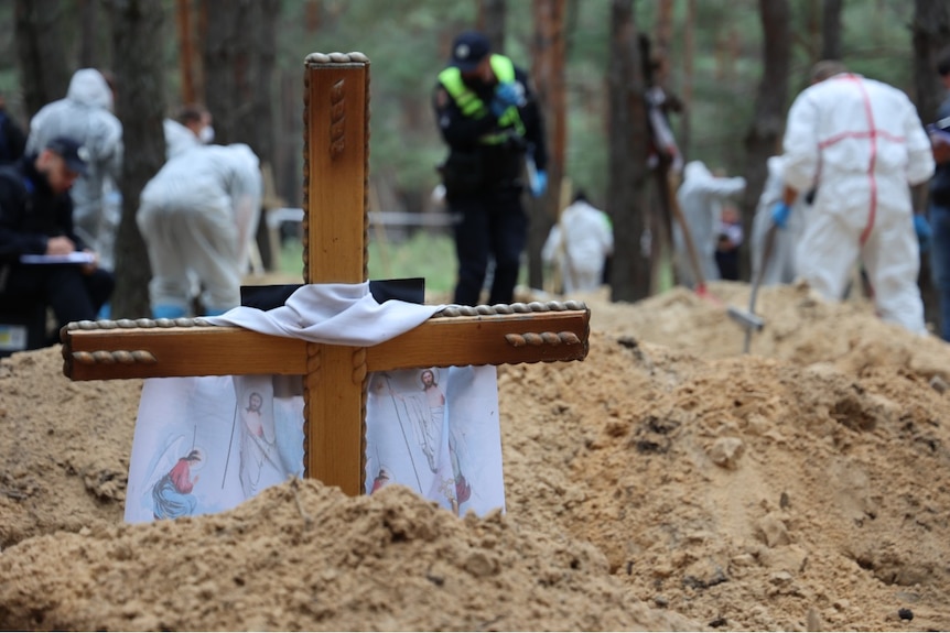 People wearing protective clothing can be seen working behind a wooden cross in the ground.