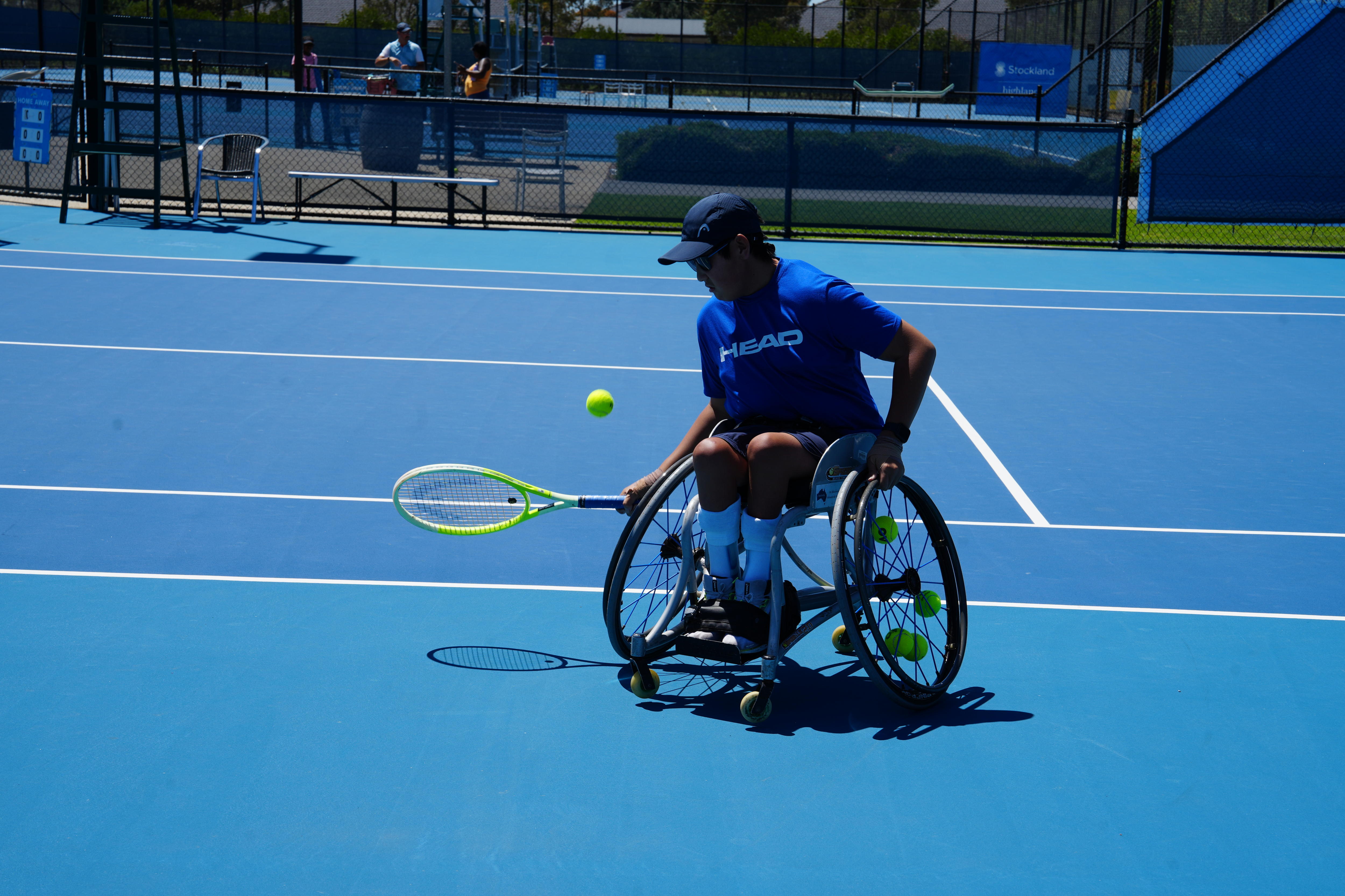 Jin Woodman is on a blue tennis court, racing to hit a ball is his wheelchair.