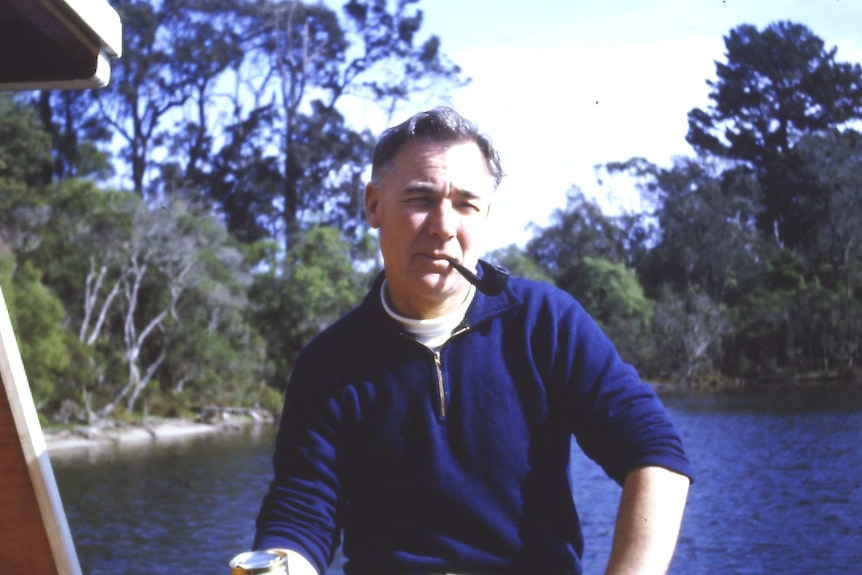 WWII veteran Bill Rudd sits on a boat and looks at the camera while he smokes a pipe.