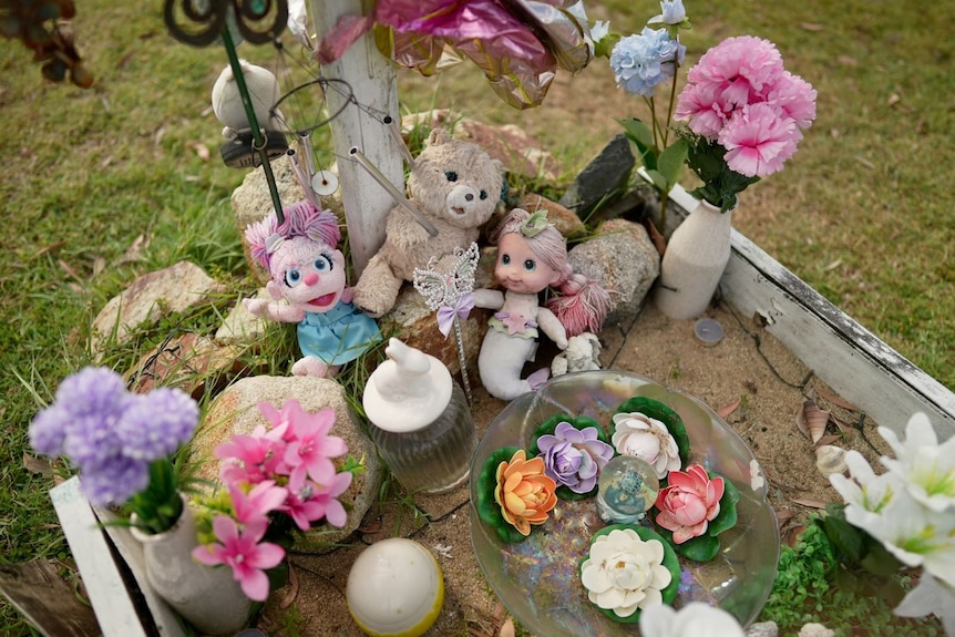 Toys and flowers sit on top of a grave.