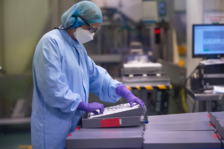 Person in mask and scrubs looking at container full of medical vials