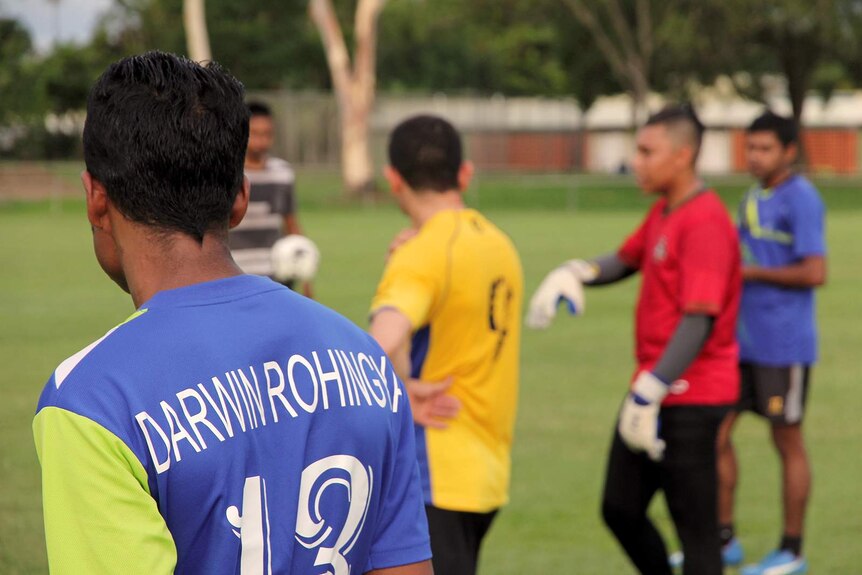 A photo on a soccer field with a person wearing a Darwin Rohingya jersey in the foreground and a soccer ball in the background.
