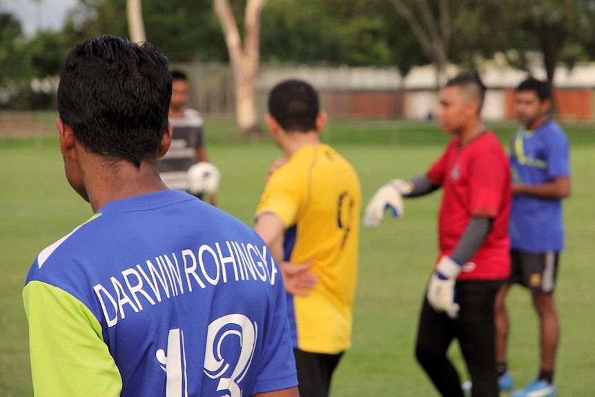 A photo on a soccer field with a person wearing a Darwin Rohingya jersey in the foreground and a soccer ball in the background.