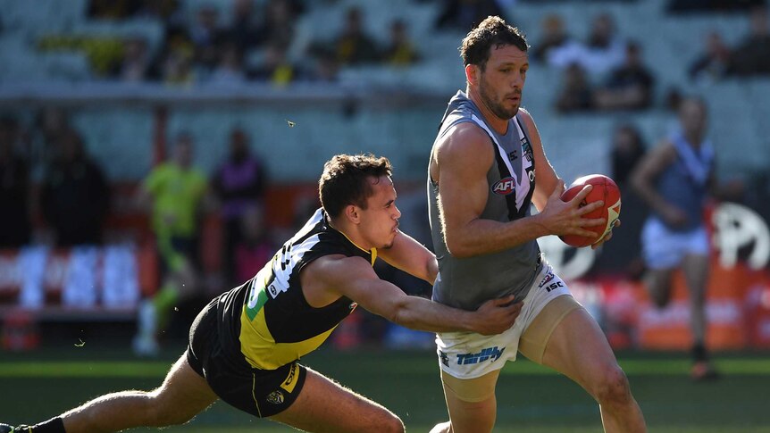 Sydney Stack, legs outstretched and arms around Travis Boak's waist, tackles his opponent