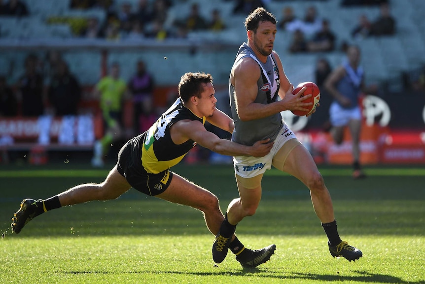 Sydney Stack, legs outstretched and arms around Travis Boak's waist, tackles his opponent