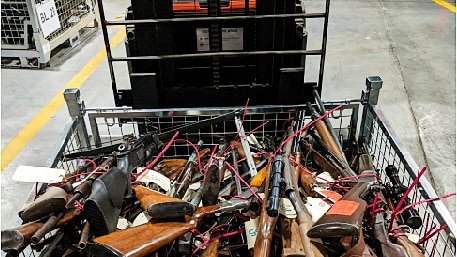 dozens of rifles and a crossbow stacked on top of each other