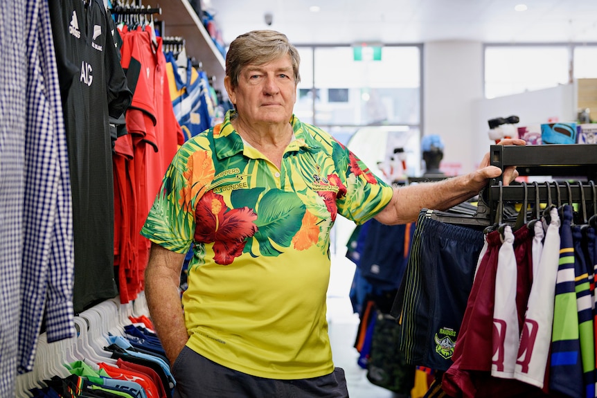 An elderly man looks at the camera in a footy shop