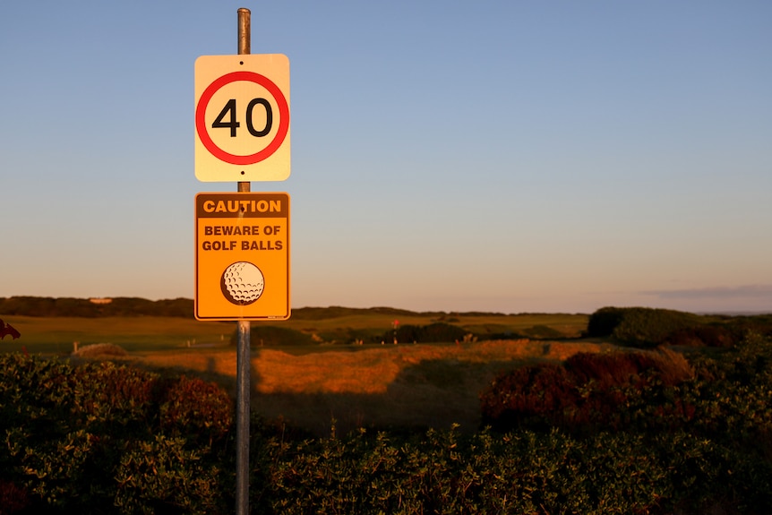 A 40km/h road sign with a Caution Beware of Golf Balls sign, at sunset with a golf course in background
