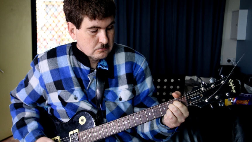 A man playing guitar at home in his unit