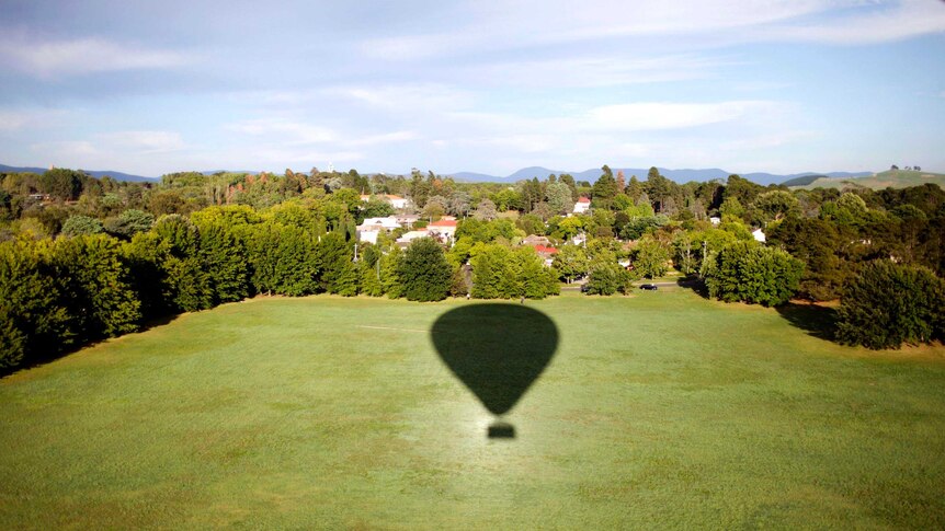 Shadow of a hot air balloon on a patch of grass.