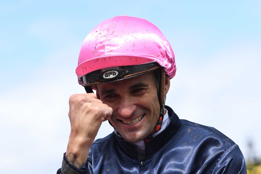 Jockey wearing pink helmet and navy top smiles and makes fist to celebrate win