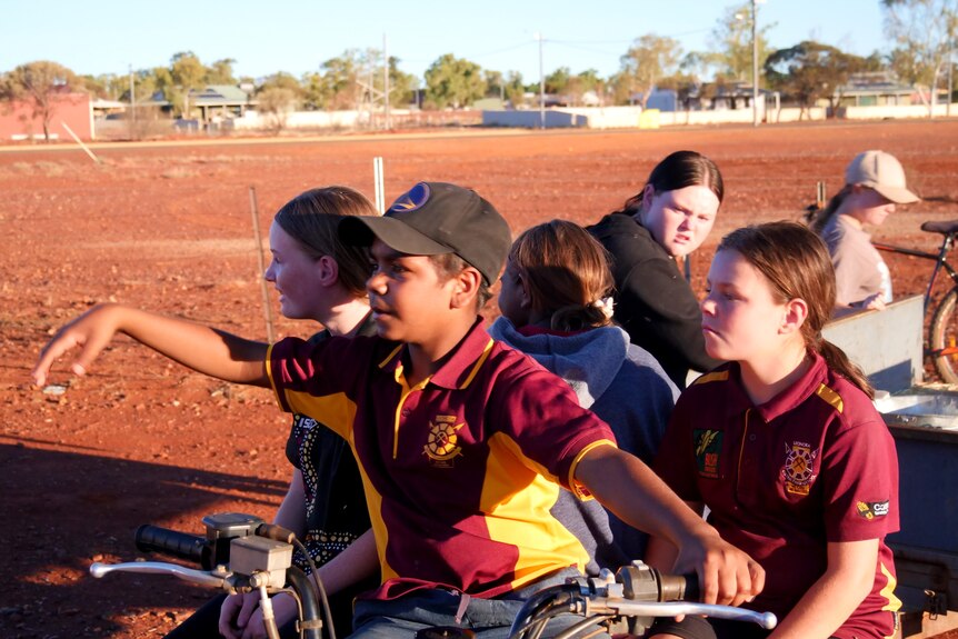 Six kids at Prickle Patch farm in Western Australia's Leonora as they ride upon a farm bike and trailer. 