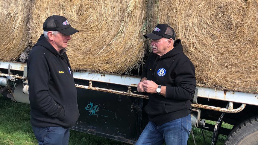 Graham Cockerell and Don Petty stand talking next to a truck of hay.