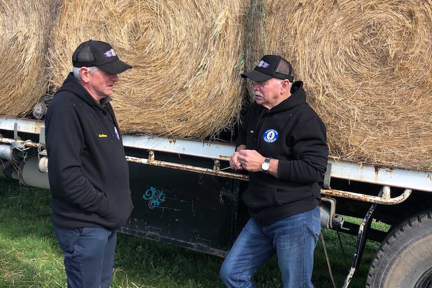 Graham Cockerell and Don Petty stand talking next to a truck of hay.