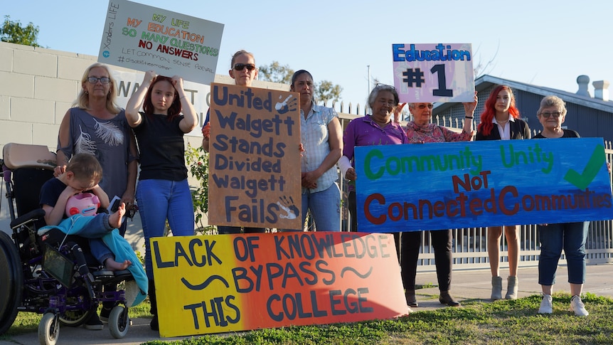 A group of people stand with protest signs outside a school building