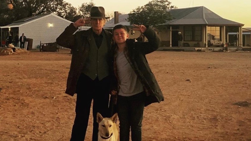 Actors stand under a sign saying 'Buckley's Chance' on a film set in the outback