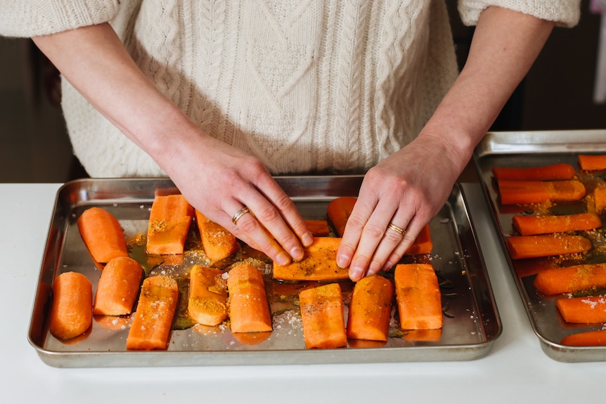 Carrot chunks being mixed with spices and olive oil on a roasting tray before baking, demonstrated by Heidi Sze.