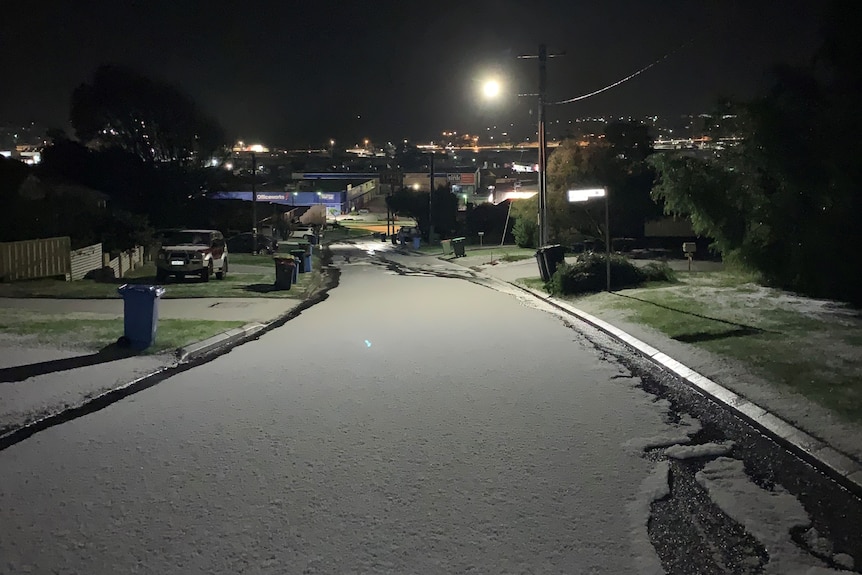 Hail blankets a suburban street, turning it white.