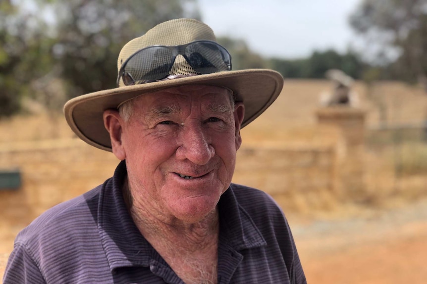 An older man in an akubra stands against a dusty farm road.