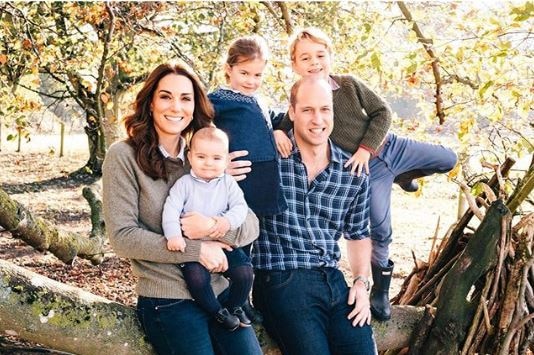 Kate holds Louis on her lap as Charlotte stands between her and William, with George on the other side. They rest on a tree.