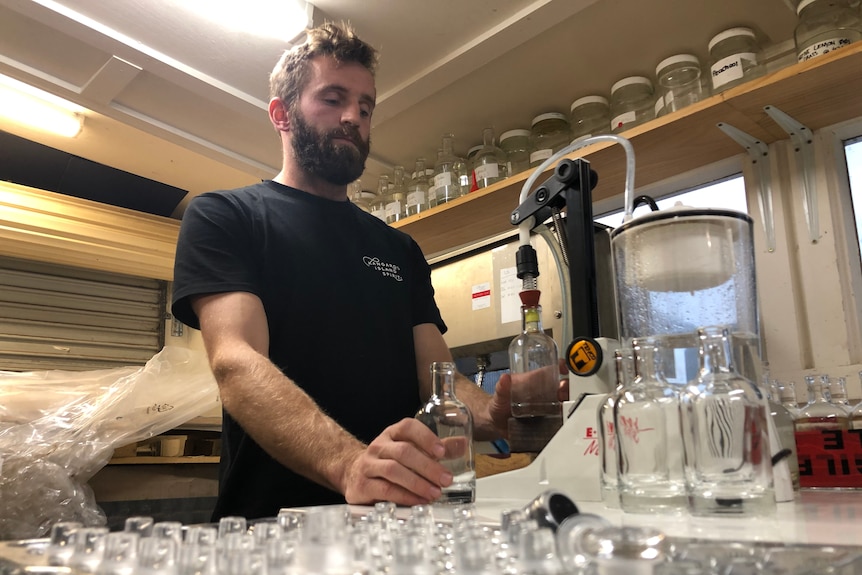 A man in a black shirt bottling some gin.