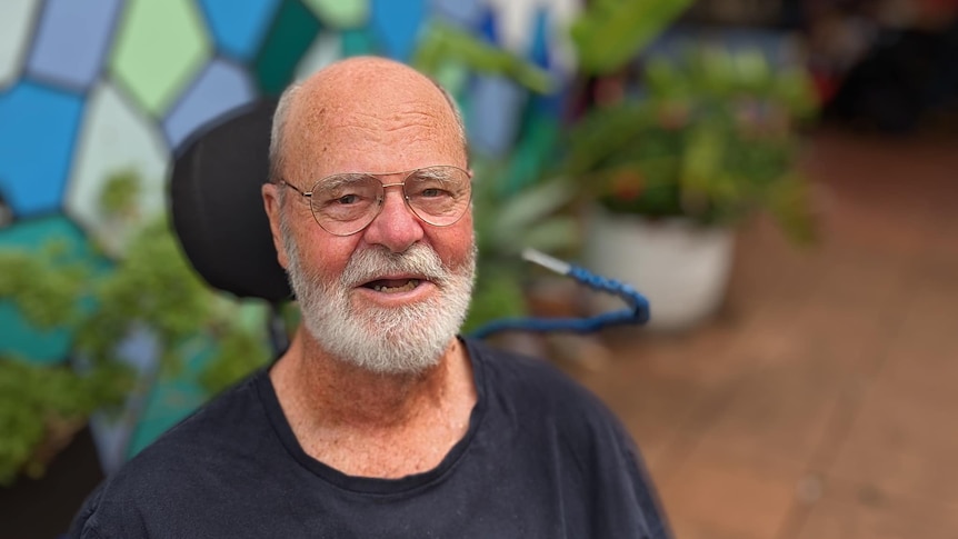 Man with white beard and glasses sitting in a wheelchair. 