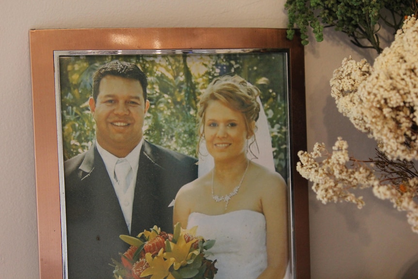 A framed wedding photo of a man and woman next to some flowers on a mantle