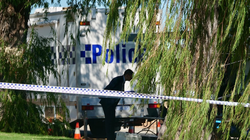 A detective at the rear of a mobile police van in front of police tape.