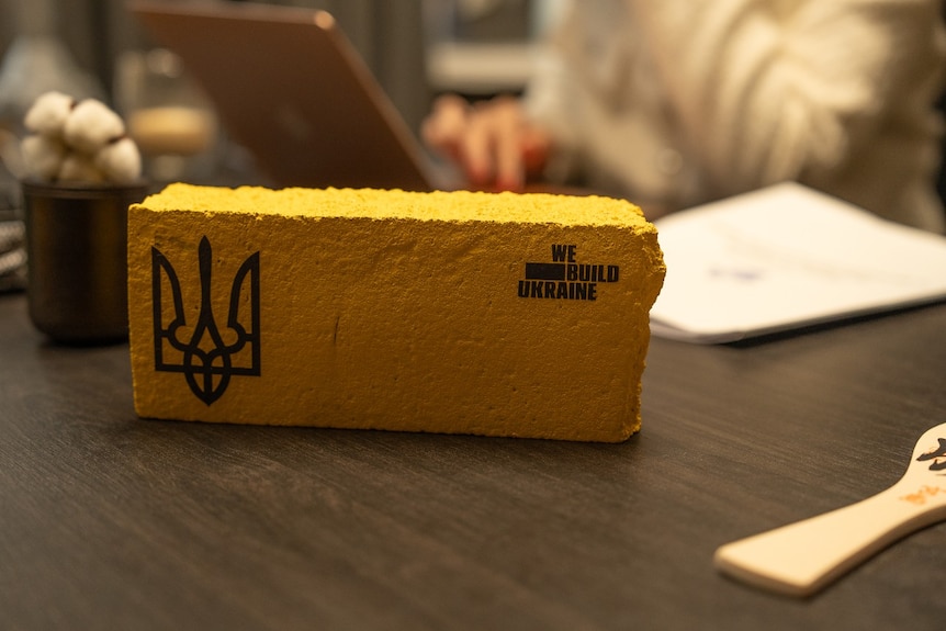 A decorative brick that says "we build Ukraine" on it on a desk 