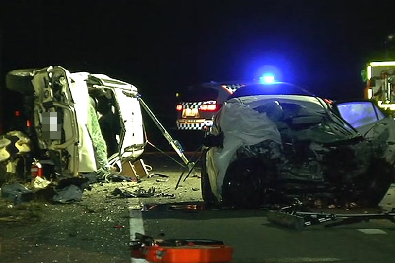 Two crashed cars, one on its side on the guardrail. A police and fire services vehicles sit nearby.