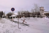 The snow-covered entrance to a Russian prison camp, showing road barriers and guard towers.