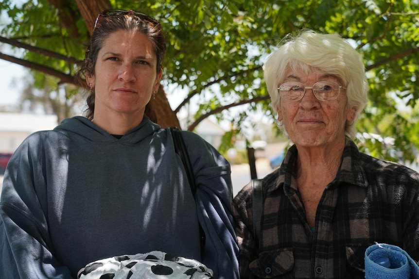 an adult daughter and her elderly mother standing beside each other looking straight at the camera with straight faces