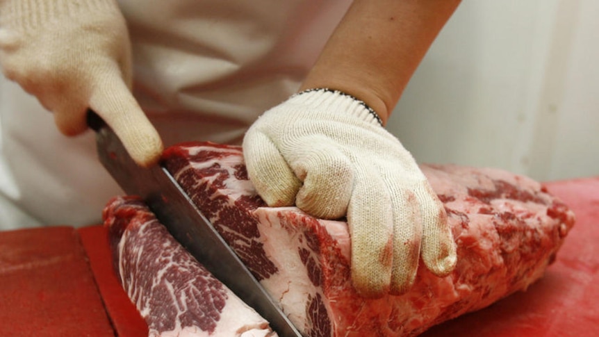 A butcher cuts beef at a market.