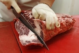 A butcher cuts beef at a market.