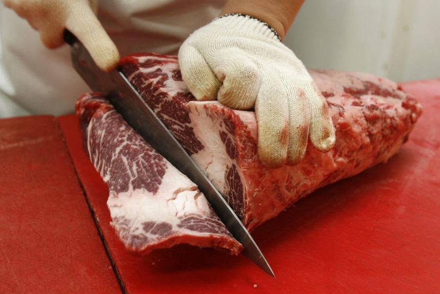 A butcher cuts beef at a market.