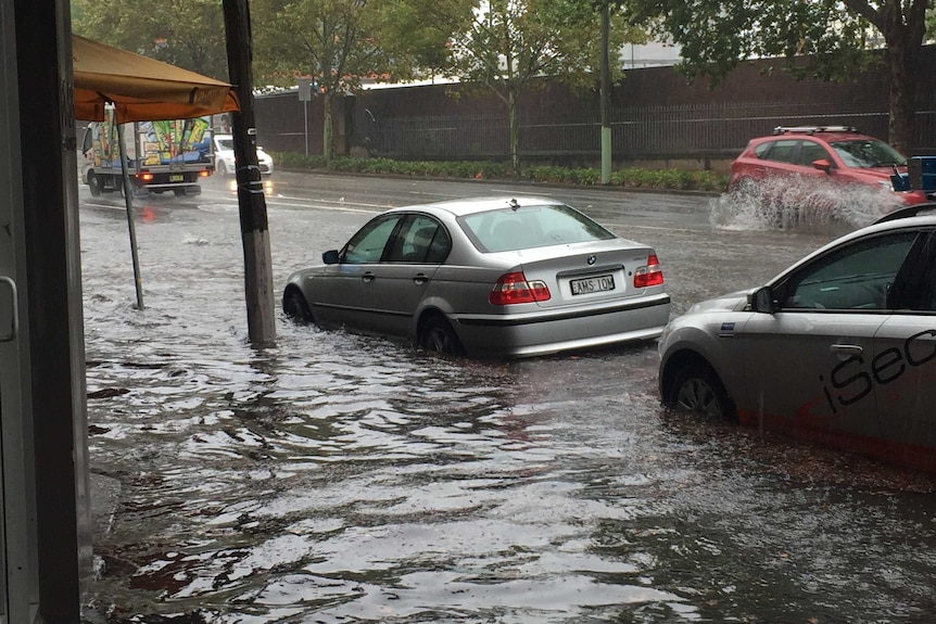 Floodwaters surround a silver car parked on a busy Sydney street.