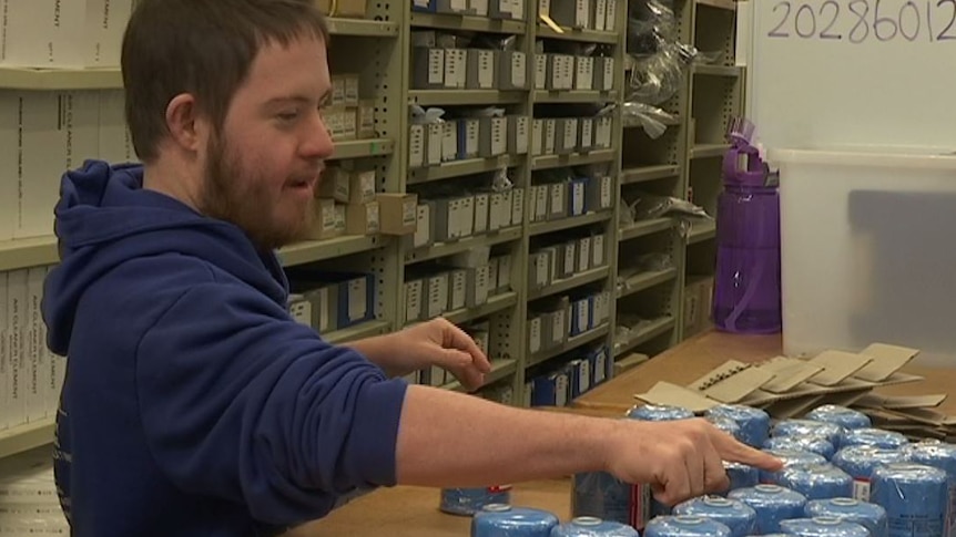 Josh Meredith in blue jumper counting packs on counter in mechanics shop