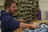 Josh Meredith in blue jumper counting packs on counter in mechanics shop