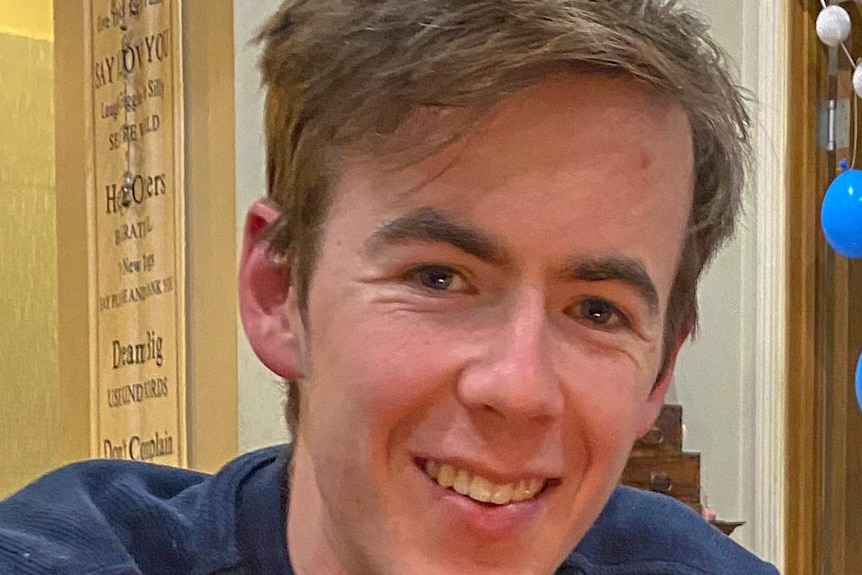 A young man with blonde curly hair smiles at the camera