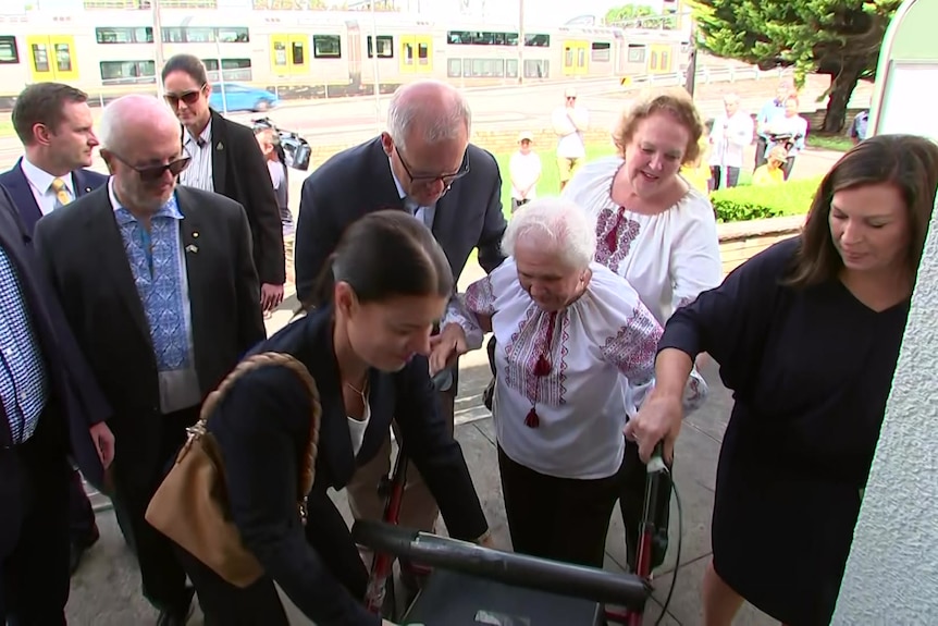 Scott Morrison helps an old woman with a walker up a set of stairs.