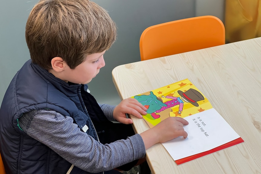 A young boy wearing a dark blue shirt reading a book. 