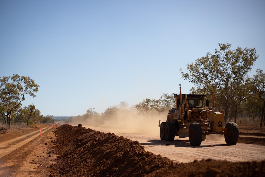 A roadworks vehicle drives along a dirt road being repaired.