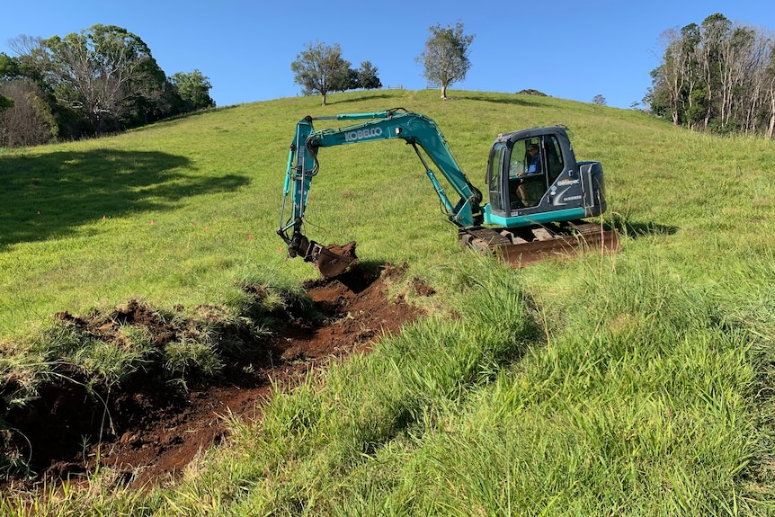A man in a green excavator digging a contour on a farm.